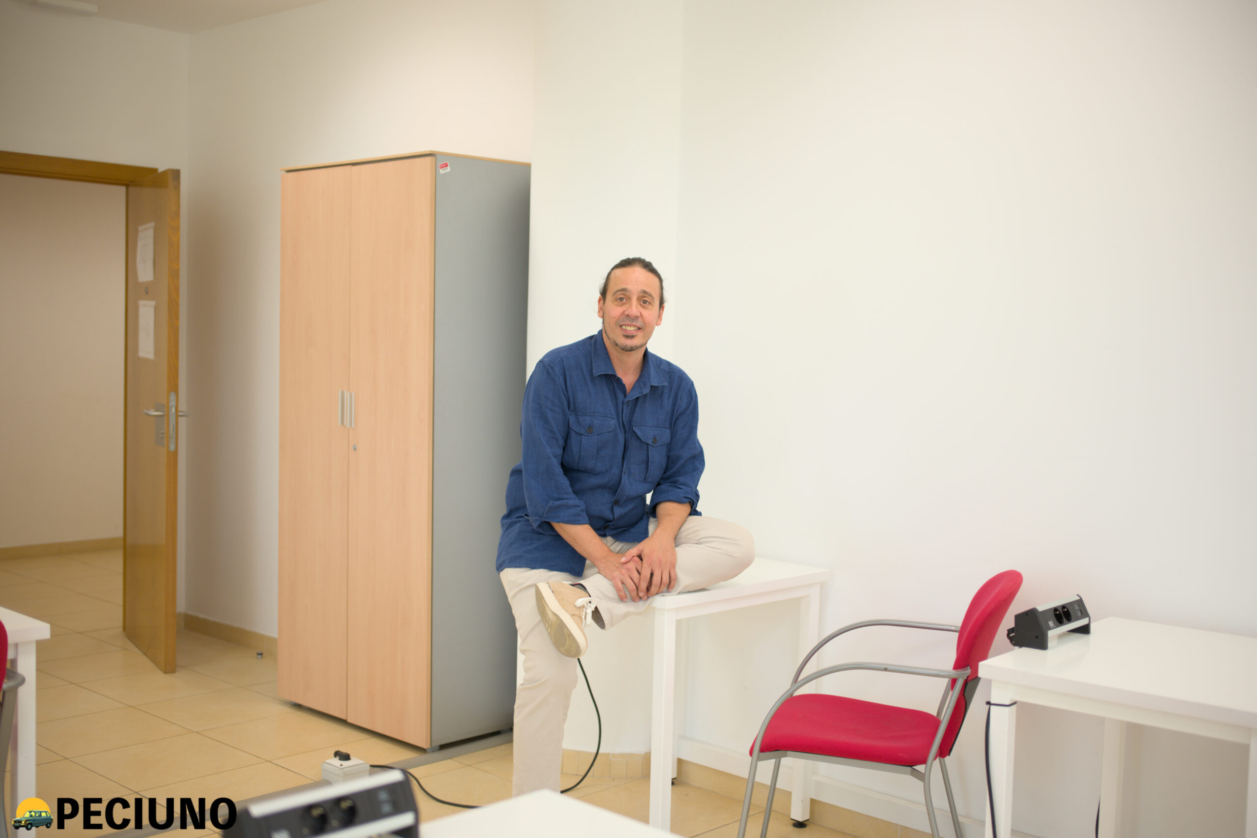 Kike de los Reyes con camisa azul sentado en una mesa de una clase